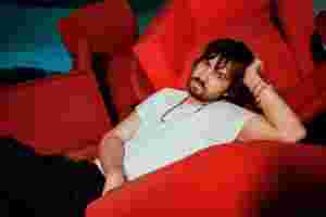 Kevin Parker of Tame Impala, captured in a moment of relaxed contemplation on vibrant red seating.